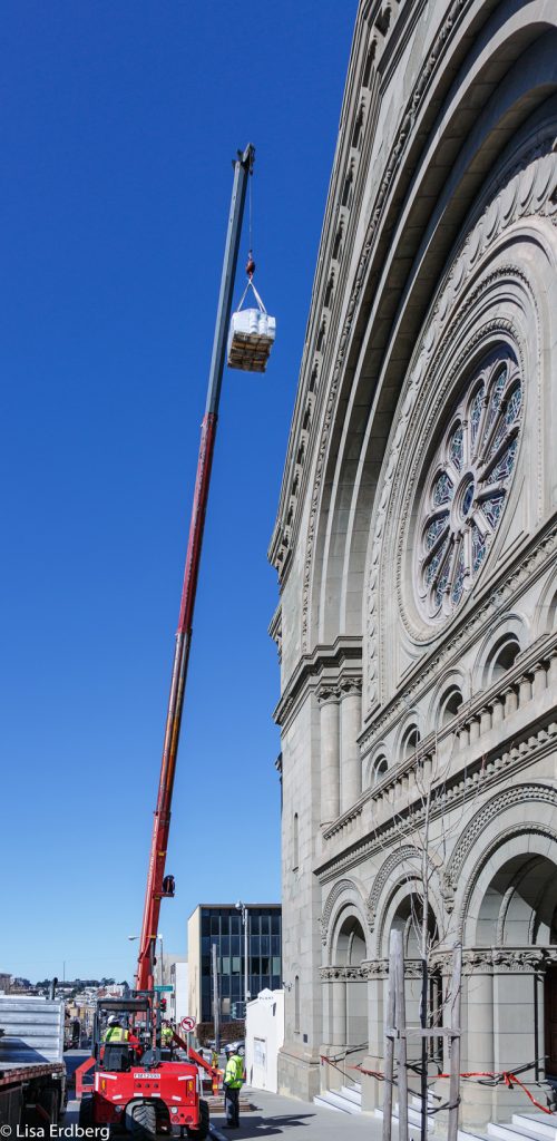 A crane hoists roofing material to the temple's historic dome.